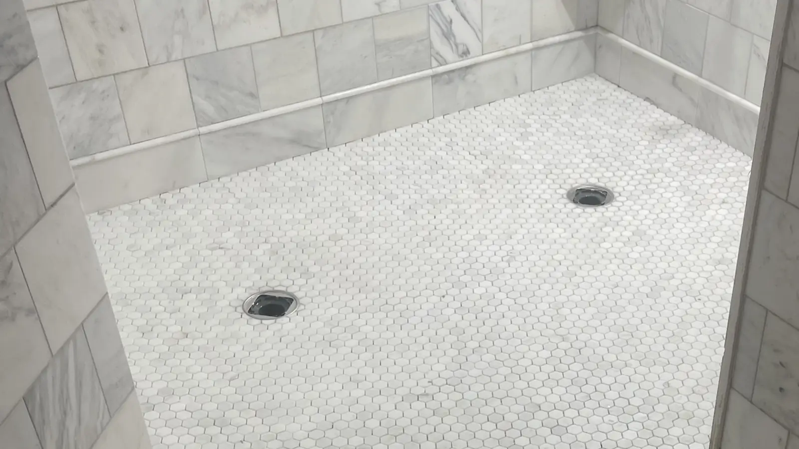 Finished marble shower with a hexagon mosaic floor and two drains